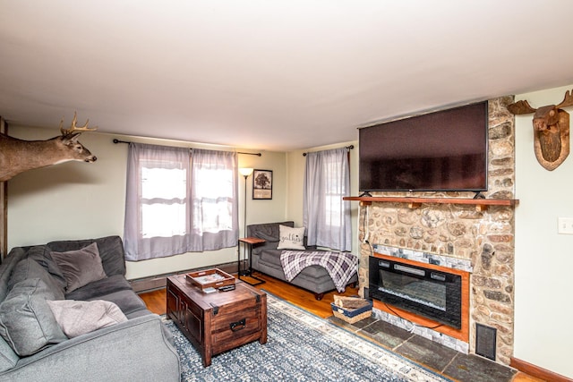 living room with hardwood / wood-style flooring, a baseboard radiator, and a stone fireplace