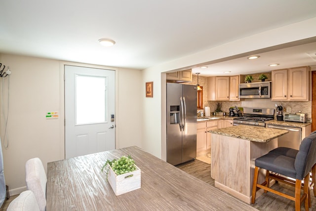 kitchen with a breakfast bar area, appliances with stainless steel finishes, hanging light fixtures, a kitchen island, and light brown cabinetry