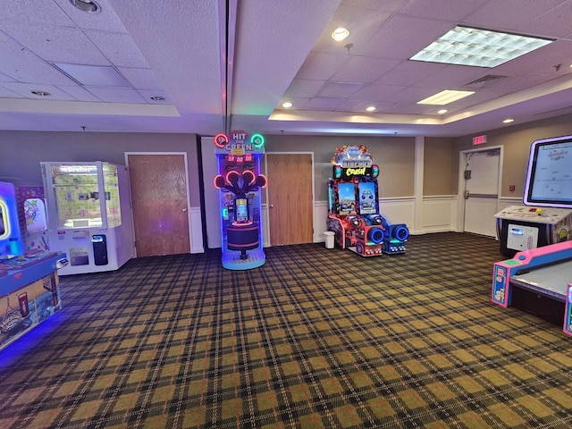 rec room with a raised ceiling, a drop ceiling, and dark carpet