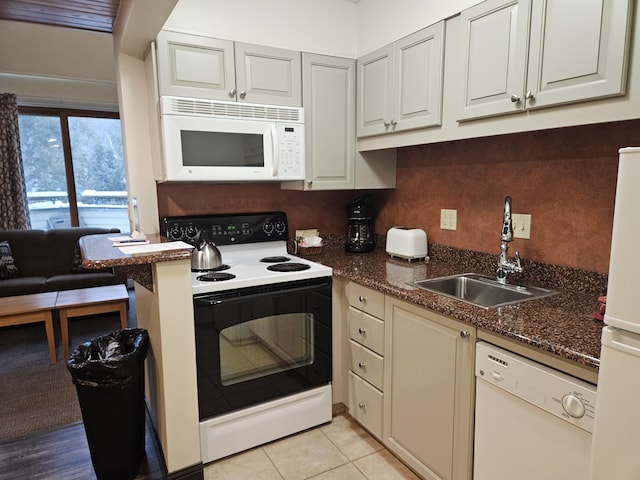 kitchen featuring sink, light tile patterned floors, white appliances, and dark stone counters