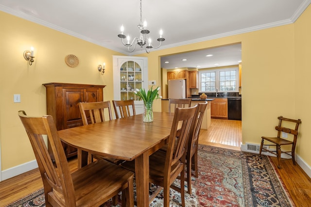 dining space with crown molding, sink, a chandelier, and light hardwood / wood-style floors