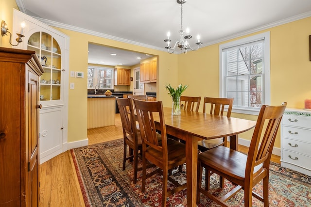 dining room featuring sink, a notable chandelier, light hardwood / wood-style flooring, and ornamental molding