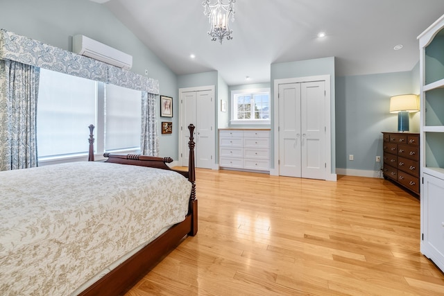 bedroom featuring lofted ceiling, light hardwood / wood-style flooring, an AC wall unit, multiple closets, and a notable chandelier