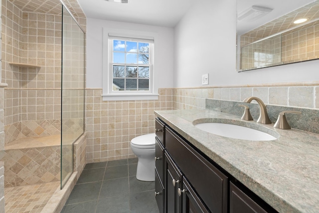 bathroom with tile patterned floors, toilet, an enclosed shower, tile walls, and vanity