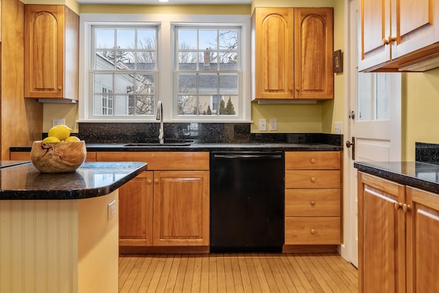 kitchen with dark stone countertops, sink, light hardwood / wood-style flooring, and black dishwasher