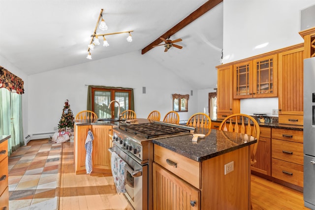 kitchen featuring appliances with stainless steel finishes, vaulted ceiling with beams, dark stone counters, a center island, and light hardwood / wood-style floors