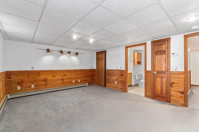 spare room featuring light carpet, a baseboard heating unit, wooden walls, and a drop ceiling