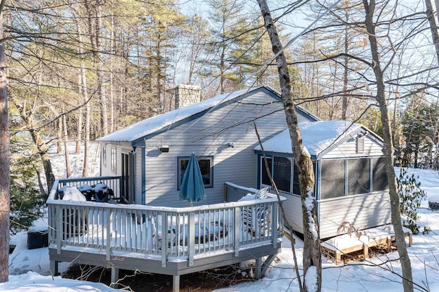 snow covered back of property featuring a deck and a sunroom