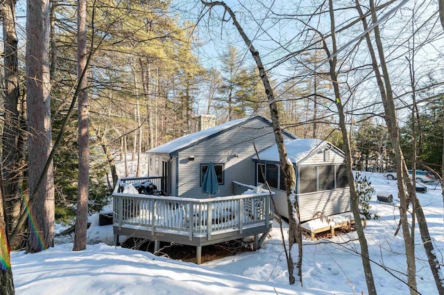 snow covered back of property featuring a deck and a sunroom