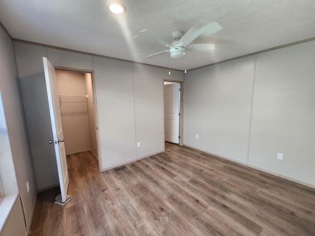 unfurnished bedroom with crown molding, light hardwood / wood-style flooring, a textured ceiling, a spacious closet, and a closet