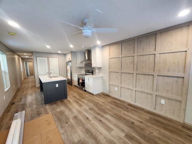 kitchen featuring sink, stainless steel range with electric cooktop, an island with sink, white cabinets, and wall chimney range hood