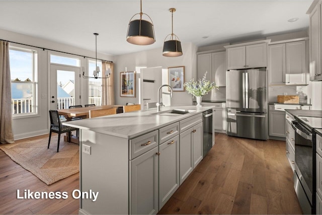 kitchen with appliances with stainless steel finishes, sink, a kitchen island with sink, and hanging light fixtures