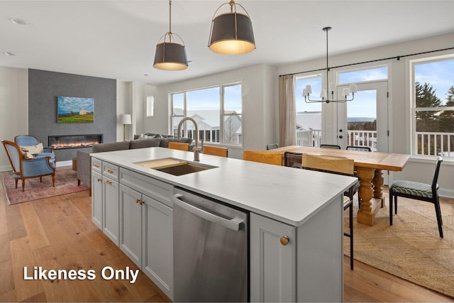 kitchen with sink, dishwasher, hanging light fixtures, light hardwood / wood-style floors, and a center island with sink