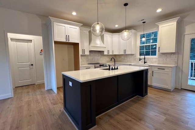 kitchen with white cabinets, light wood-type flooring, custom range hood, and a sink