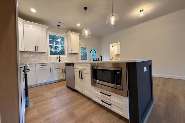 kitchen with backsplash, light countertops, light wood-style flooring, stainless steel appliances, and white cabinetry