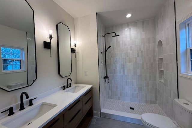 full bathroom featuring a sink, tiled shower, toilet, and double vanity