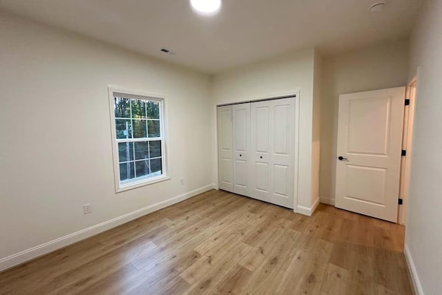 unfurnished bedroom with light wood-type flooring, baseboards, visible vents, and a closet