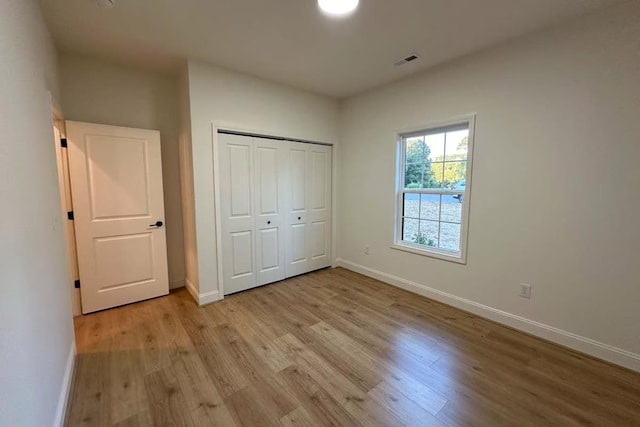 unfurnished bedroom featuring light wood-type flooring, visible vents, baseboards, and a closet