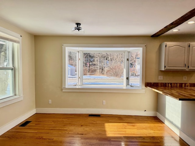 unfurnished dining area featuring beam ceiling and light wood-type flooring