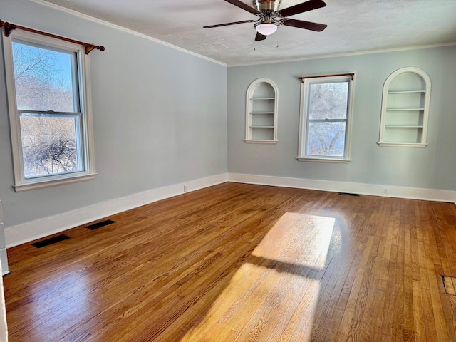 unfurnished room featuring crown molding, a textured ceiling, built in features, hardwood / wood-style flooring, and ceiling fan