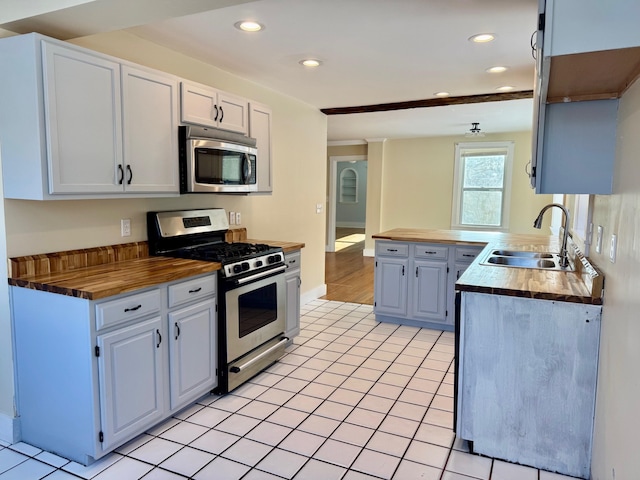 kitchen with sink, butcher block countertops, white cabinetry, light tile patterned floors, and appliances with stainless steel finishes