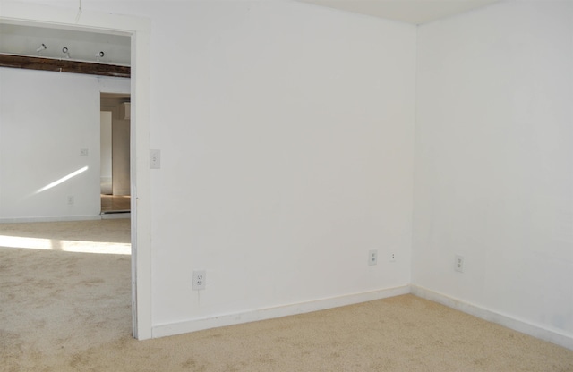 spare room featuring light carpet and baseboards