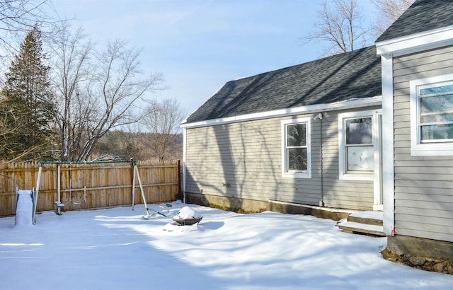 view of snow covered exterior featuring an outdoor fire pit, a shingled roof, and fence