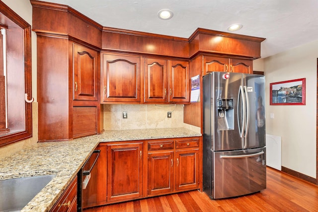 kitchen featuring light wood-type flooring, stainless steel fridge with ice dispenser, sink, light stone counters, and decorative backsplash