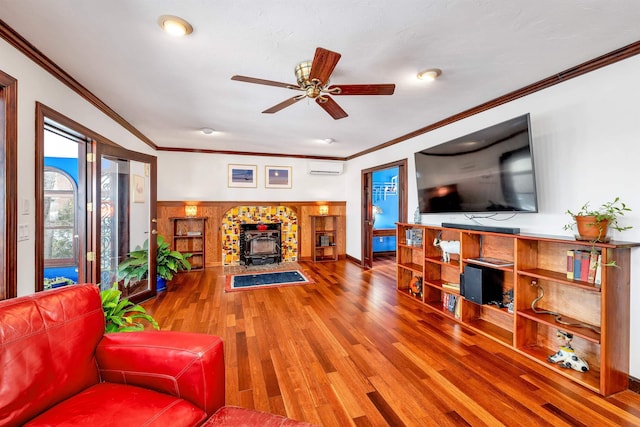 living room with a wood stove, ceiling fan, hardwood / wood-style flooring, a wall mounted AC, and ornamental molding