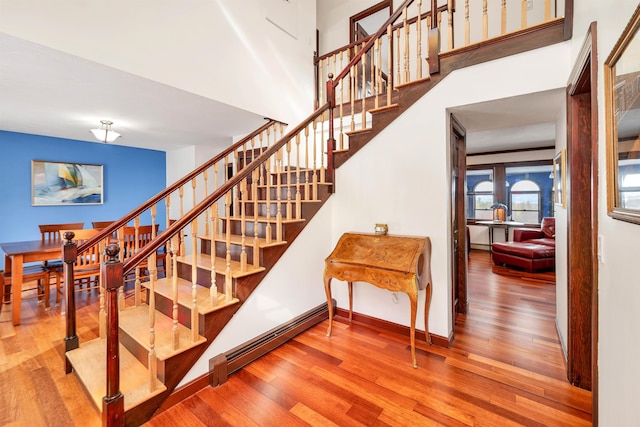 staircase featuring wood-type flooring, a baseboard heating unit, and a towering ceiling