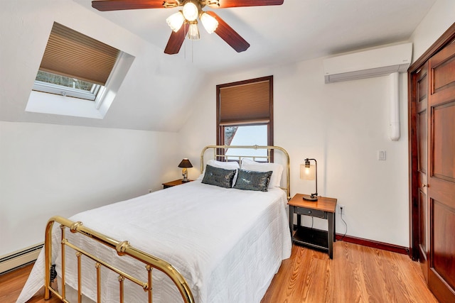 bedroom with an AC wall unit, light hardwood / wood-style flooring, lofted ceiling with skylight, ceiling fan, and a baseboard radiator