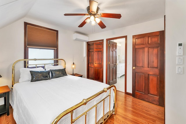 bedroom featuring light wood-type flooring, connected bathroom, ceiling fan, vaulted ceiling, and a wall unit AC