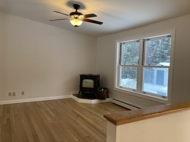 unfurnished living room featuring wood-type flooring, a baseboard heating unit, a wood stove, and ceiling fan