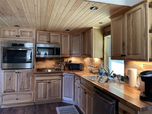 kitchen with butcher block countertops, sink, stainless steel appliances, dark hardwood / wood-style floors, and wooden ceiling