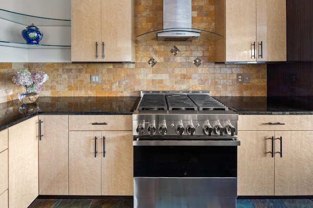 kitchen featuring stainless steel gas stove, dark stone counters, wall chimney exhaust hood, and light brown cabinets