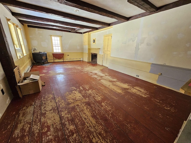 spare room with a baseboard radiator, wood-type flooring, beam ceiling, and a wood stove