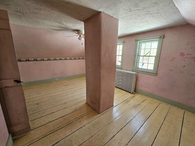 additional living space with vaulted ceiling, radiator heating unit, ceiling fan, light hardwood / wood-style floors, and a textured ceiling