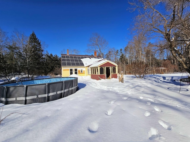 snow covered back of property featuring solar panels