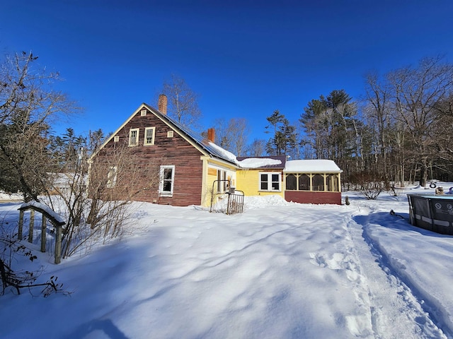 snow covered rear of property featuring a sunroom