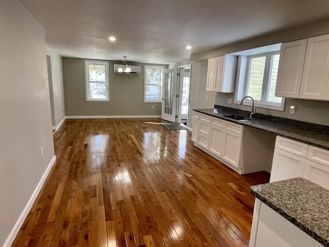 kitchen with an AC wall unit, dark hardwood / wood-style floors, white cabinetry, sink, and dark stone counters