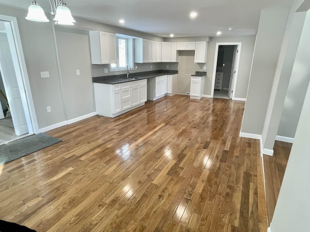 kitchen with dark hardwood / wood-style floors, sink, white cabinets, hanging light fixtures, and an inviting chandelier