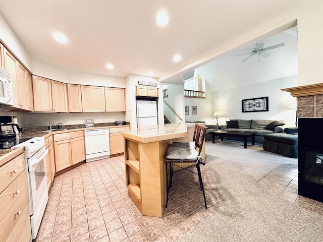 kitchen featuring lofted ceiling, light brown cabinetry, a breakfast bar, a kitchen island, and white appliances