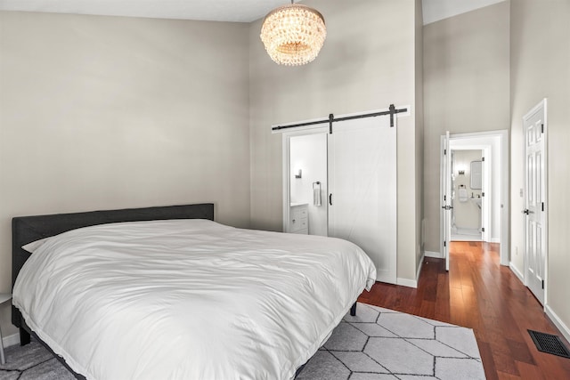 bedroom featuring ensuite bath, an inviting chandelier, a towering ceiling, dark hardwood / wood-style flooring, and a barn door