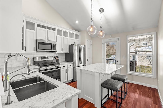 kitchen featuring sink, light stone counters, a center island, hanging light fixtures, and appliances with stainless steel finishes