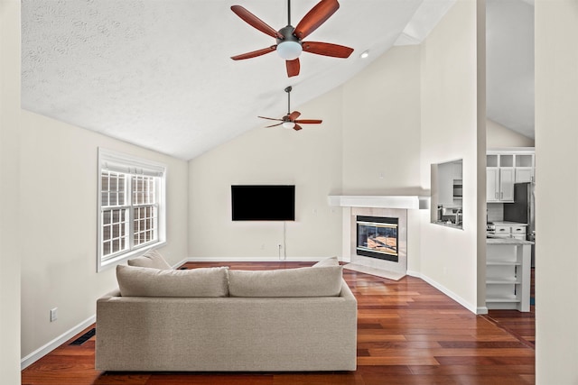 living room with ceiling fan, lofted ceiling, dark hardwood / wood-style floors, and a tiled fireplace