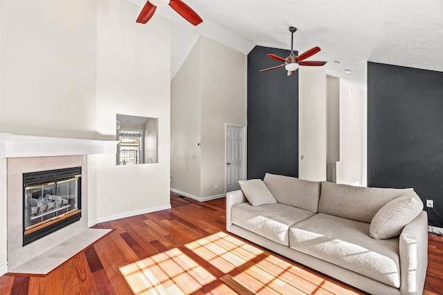 living room featuring ceiling fan, high vaulted ceiling, a tiled fireplace, and hardwood / wood-style floors