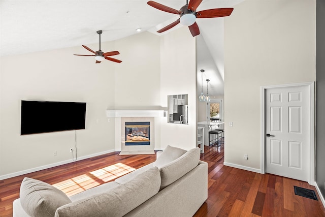 living room featuring high vaulted ceiling, a tile fireplace, dark hardwood / wood-style floors, and ceiling fan