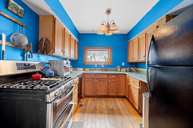 kitchen with black refrigerator, sink, range with two ovens, hanging light fixtures, and light wood-type flooring