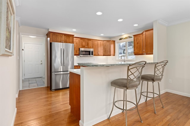 kitchen with a kitchen bar, sink, appliances with stainless steel finishes, kitchen peninsula, and light hardwood / wood-style floors