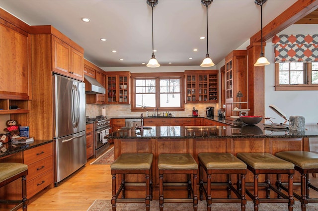 kitchen with pendant lighting, dark stone countertops, wall chimney exhaust hood, and appliances with stainless steel finishes